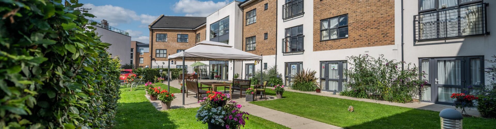 A well-maintained care home garden with a paved path leading to a seating area under a gazebo, Drayton Village Care Centre, a care home in West Drayton.