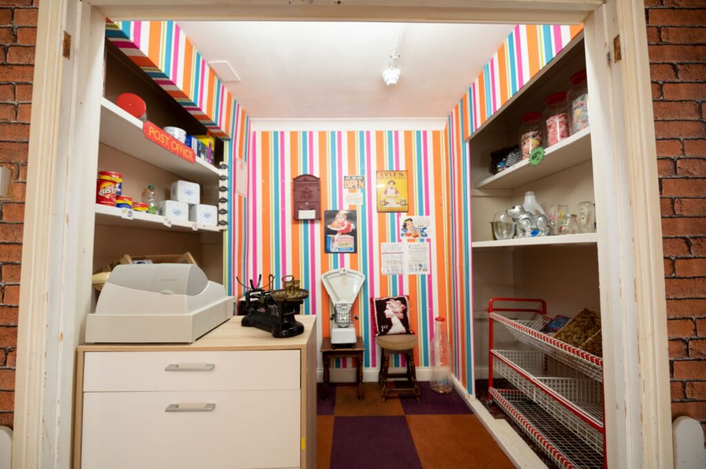 Brightly colored striped walls frame a cozy vintage-style room featuring shelves with jars, a typewriter, and nostalgic decor items.