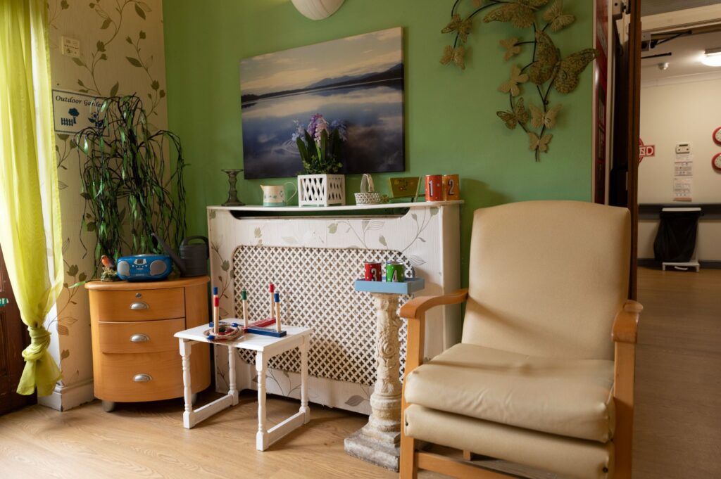 Bright green wall with floral decor, a cozy chair, wooden cabinet, small tables with toys, and a painting of a landscape.