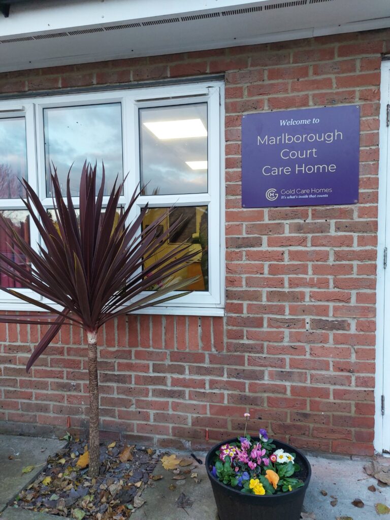 Entrance to Marlborough Court Care Home on the Thames, featuring a potted plant and a welcoming sign on the brick wall.