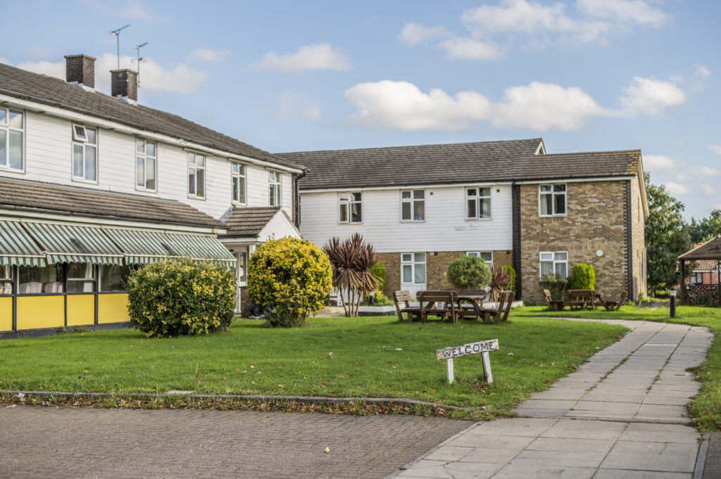 Exterior view of Hillside Nursing Home featuring a grassy area, seating, and welcoming signage, with a mix of brick and white building facades.