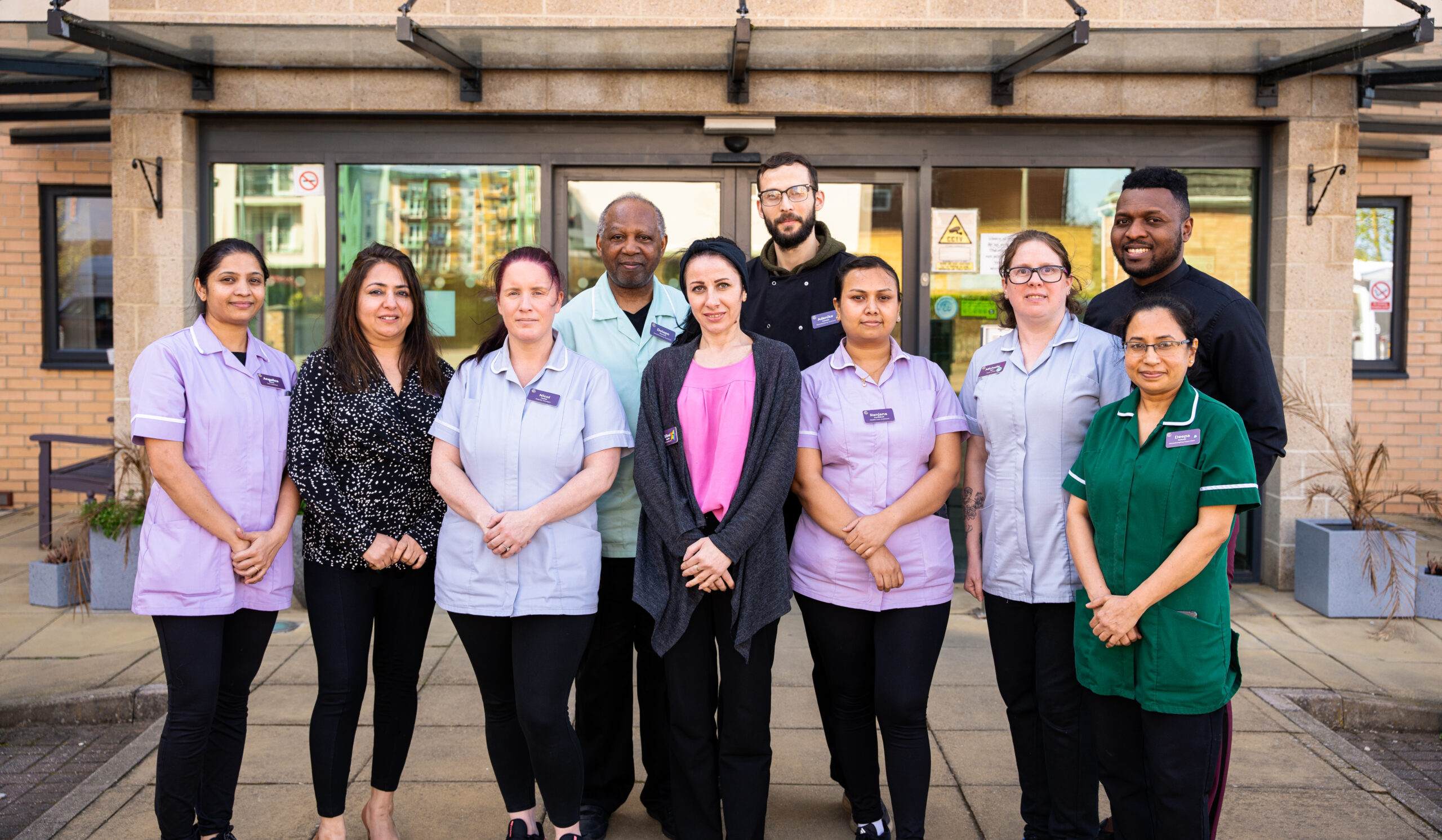 A diverse and dedicated team of care home staff standing together in front of the care home entrance, highlighting the importance of finding a good care home with a trusted team.