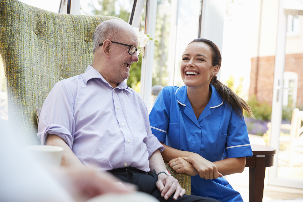 Senior man sitting in chair and talking with nurse in a retirement home, demonstrating what to expect when you find a care home.