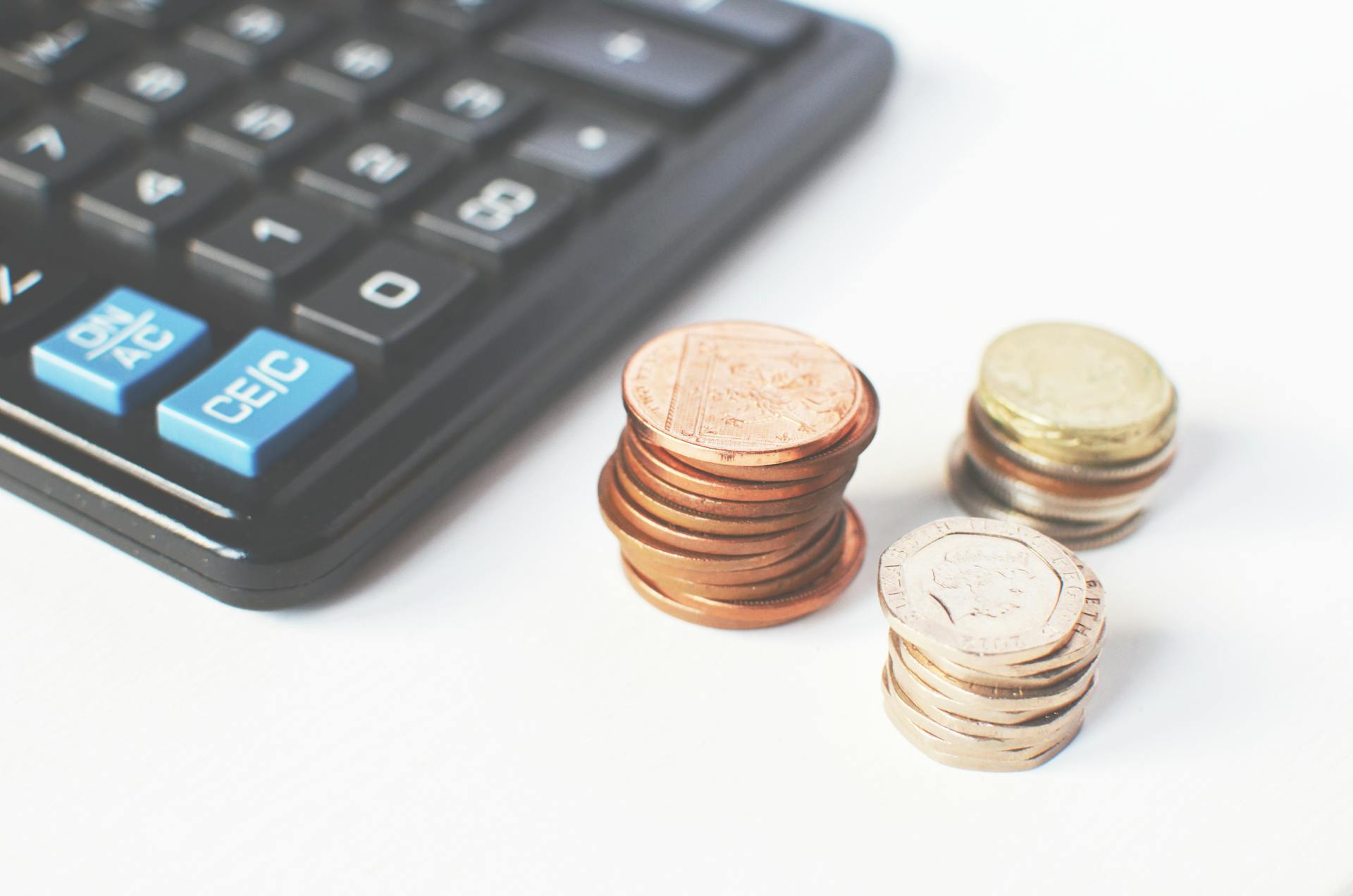 A close-up image of a calculator, accompanied by stacks of British pound coins in ascending order. This represents the financial planning involved in managing the potential care home cost.