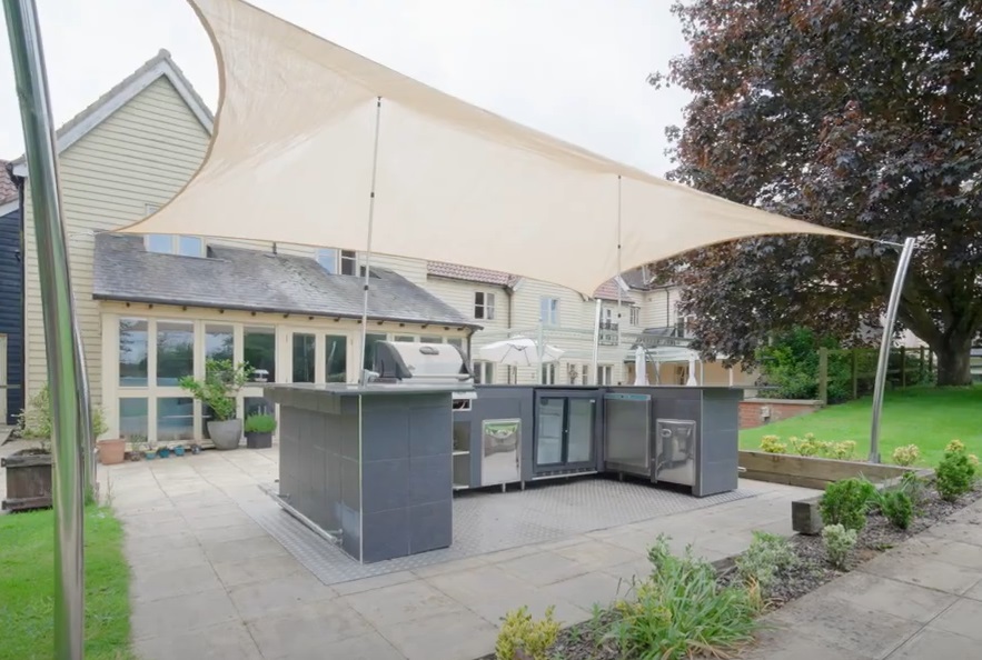 Outdoor barbecue and kitchen area at The New Deanery, featuring a shaded seating space and modern facilities for outdoor dining.