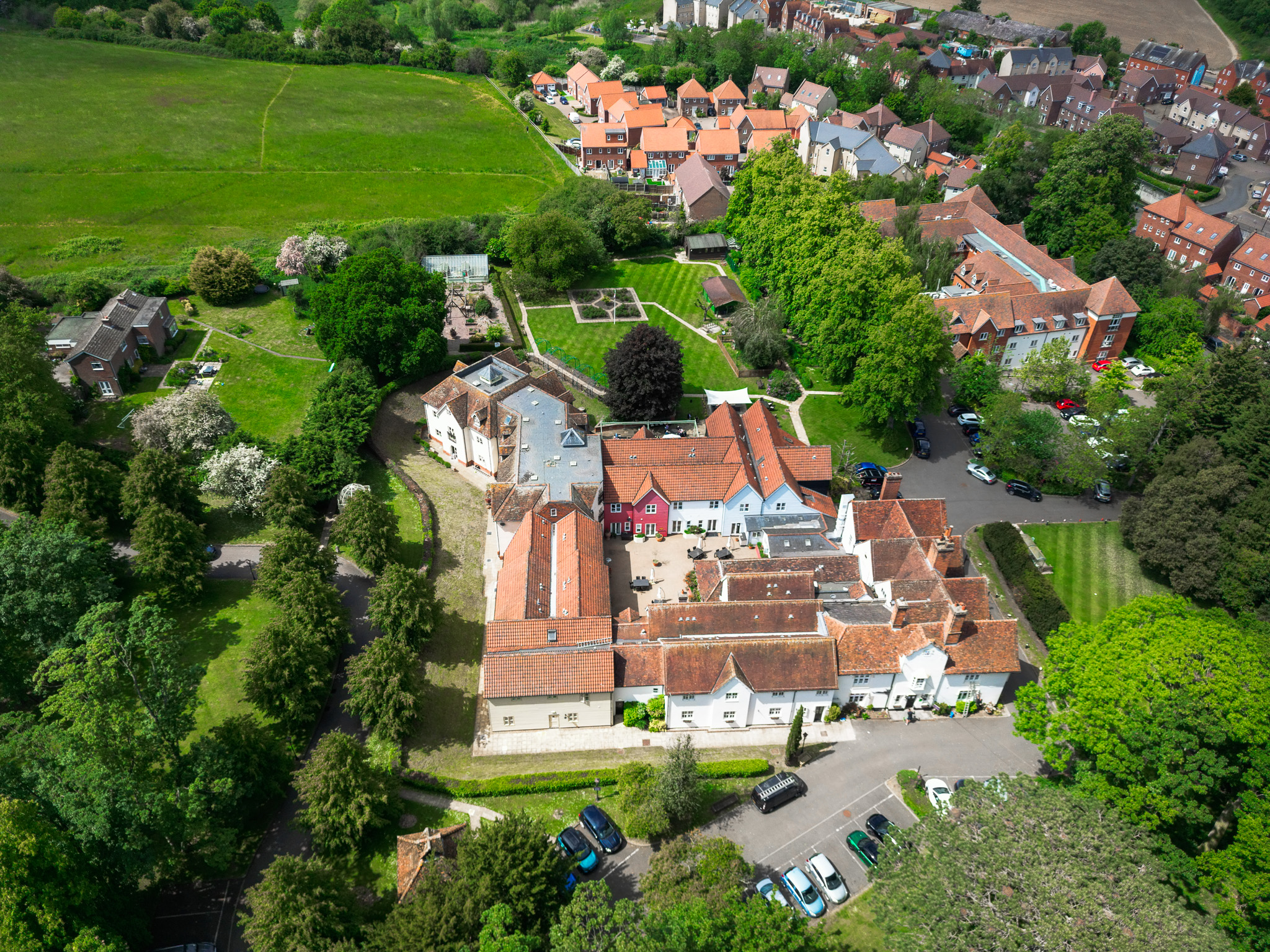 Aerial view of a care home in Braintree, surrounded by lush gardens, trees, and neighbouring houses, showcasing the spacious grounds and peaceful setting.