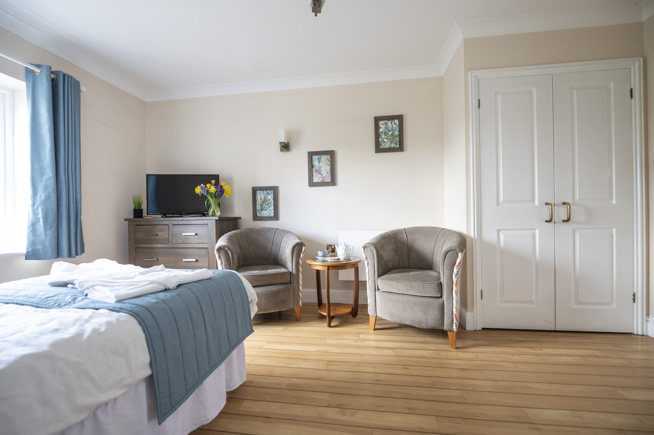 Comfortable and well-appointed bedroom at Braintree care home featuring a cosy seating area, TV, and natural light.