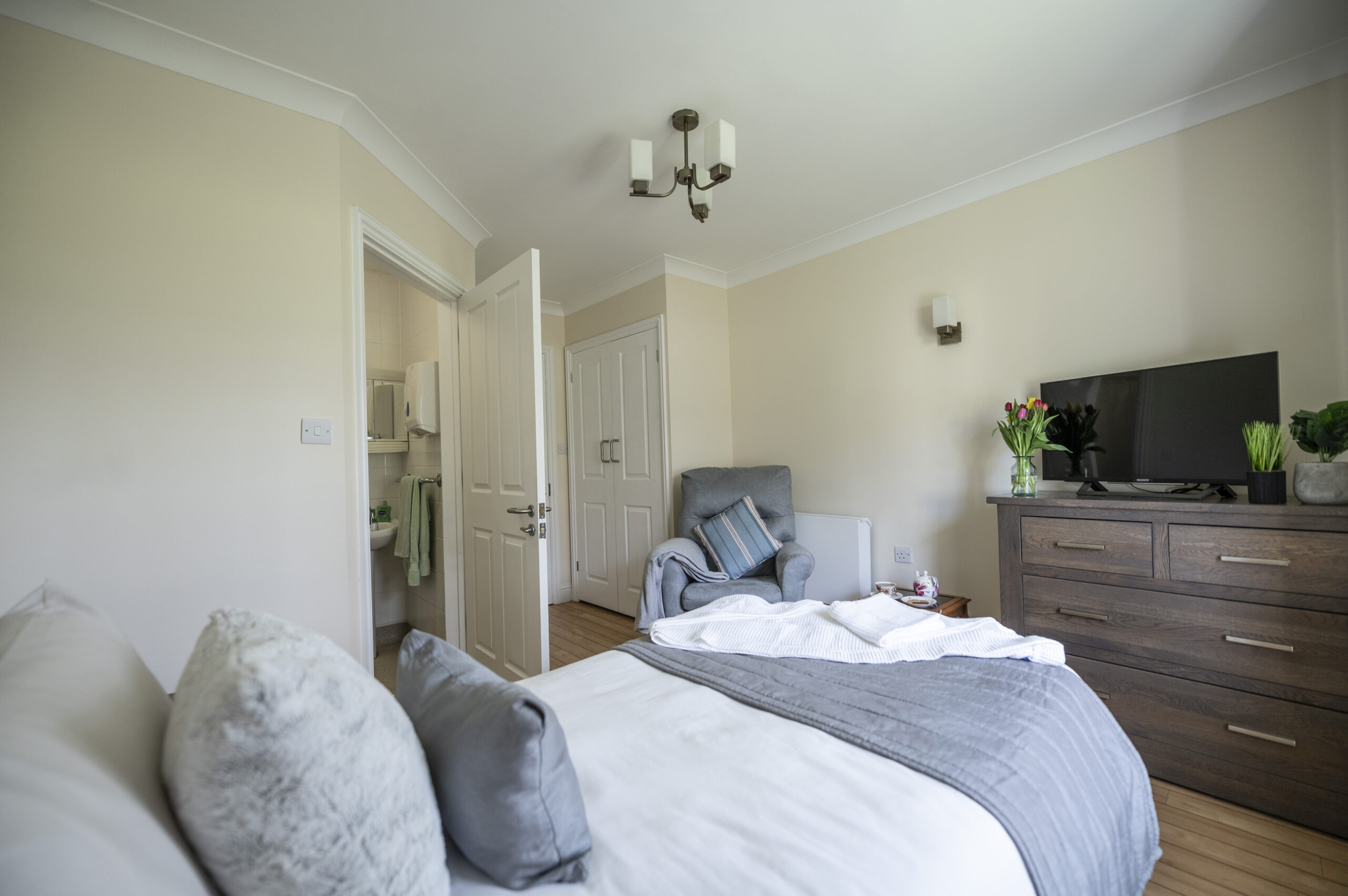 Comfortable bedroom at a care home with a bed, cosy armchair, TV, and en-suite bathroom for added privacy.