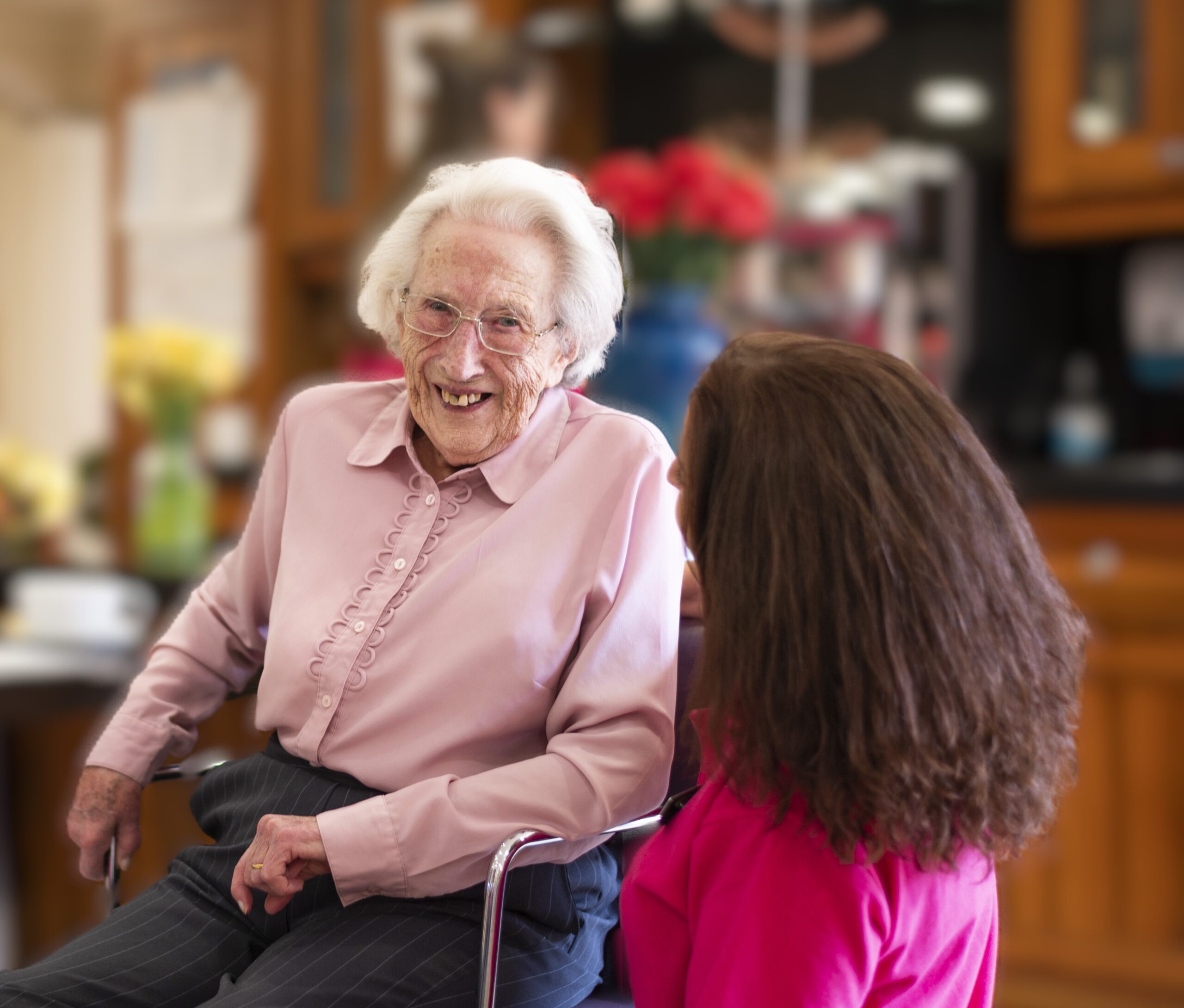 Elderly resident at a care home smiling and engaging in a warm conversation with a staff member, reflecting a friendly and supportive environment.