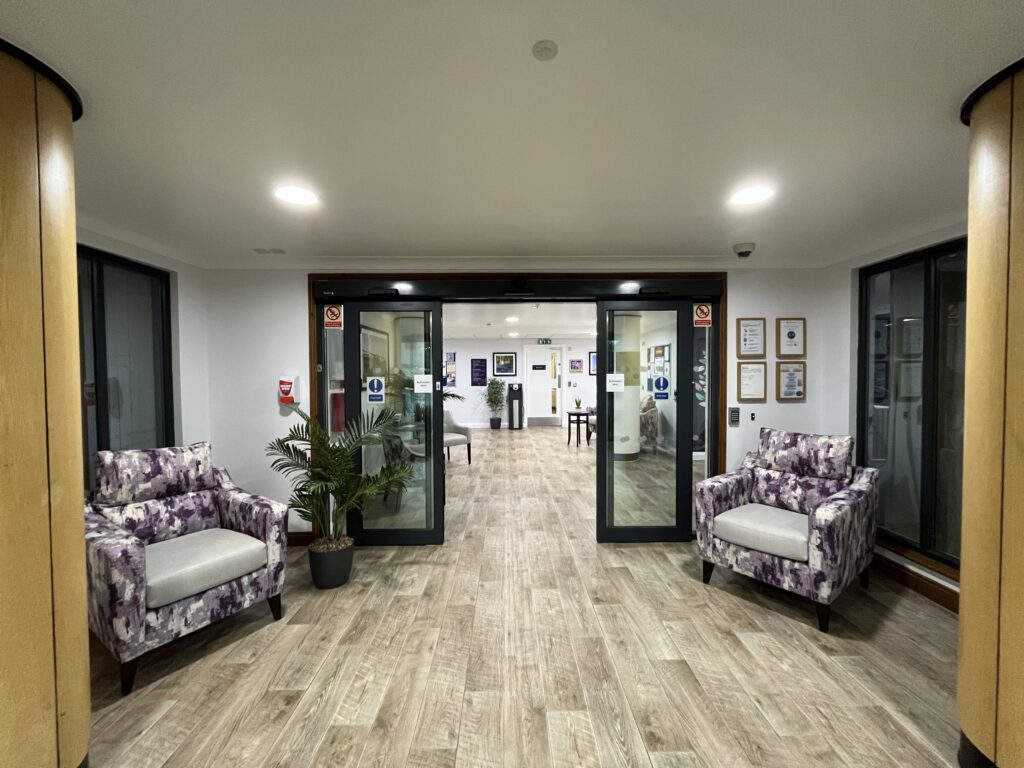 Entrance to Hatfield Nursing Home featuring cosy floral armchairs, wooden flooring, and glass doors leading into a welcoming space, a nursing home in Hatfield.