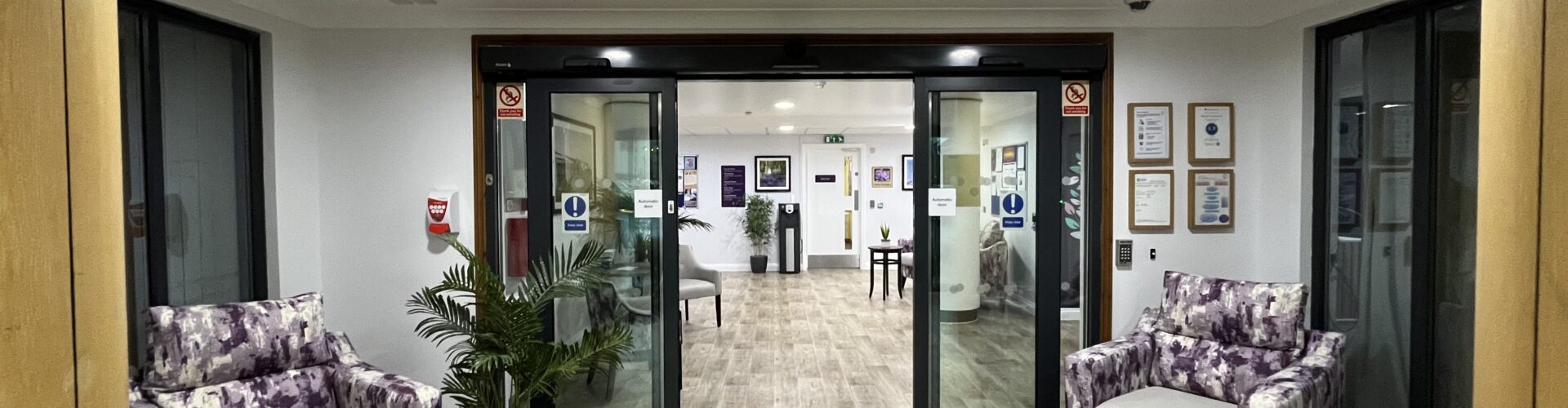 Entrance to Hatfield Nursing Home featuring cosy floral armchairs, wooden flooring, and glass doors leading into a welcoming space, a nursing home in Hatfield.