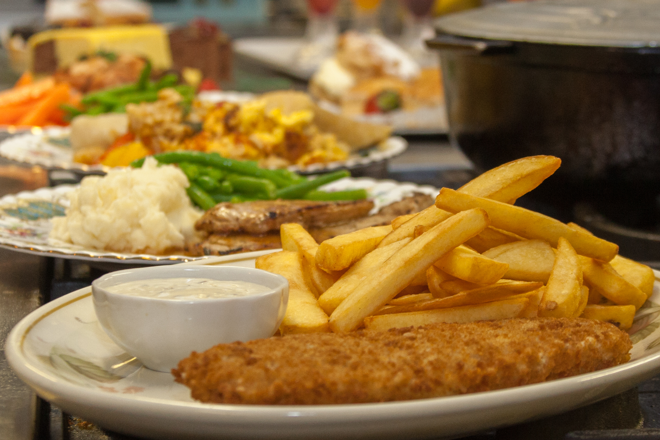 Close-up of a freshly prepared meal with fish, chips, mashed potatoes, and green beans served at a care home.