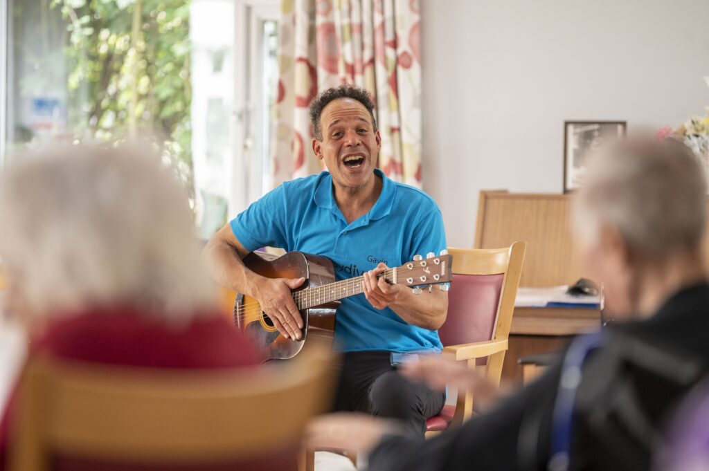 Music therapist plays guitar for residents in a care home in Hertfordshire, creating a joyful atmosphere.
