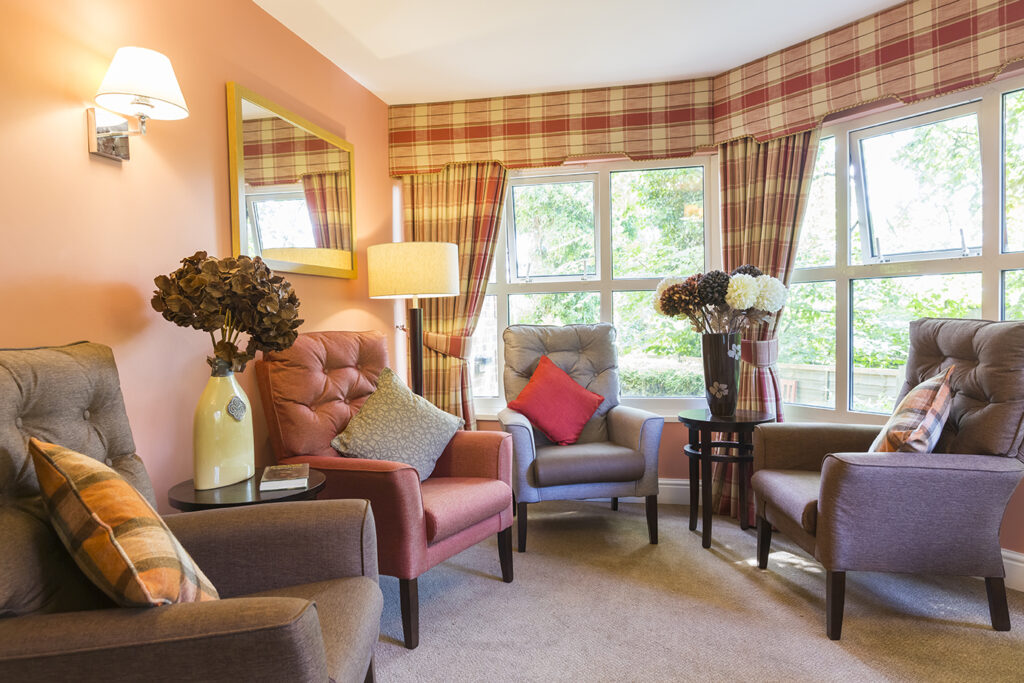 Cozy sitting area featuring armchairs, a floor lamp, and decorative flowers, with large windows dressed in plaid curtains.
