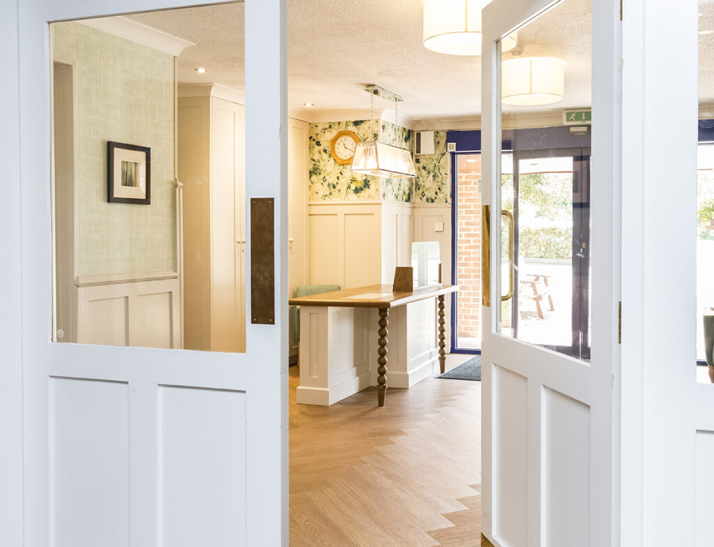 Bright interior of Kingston care home featuring a welcoming entrance, wooden table, floral wallpaper, and natural light.