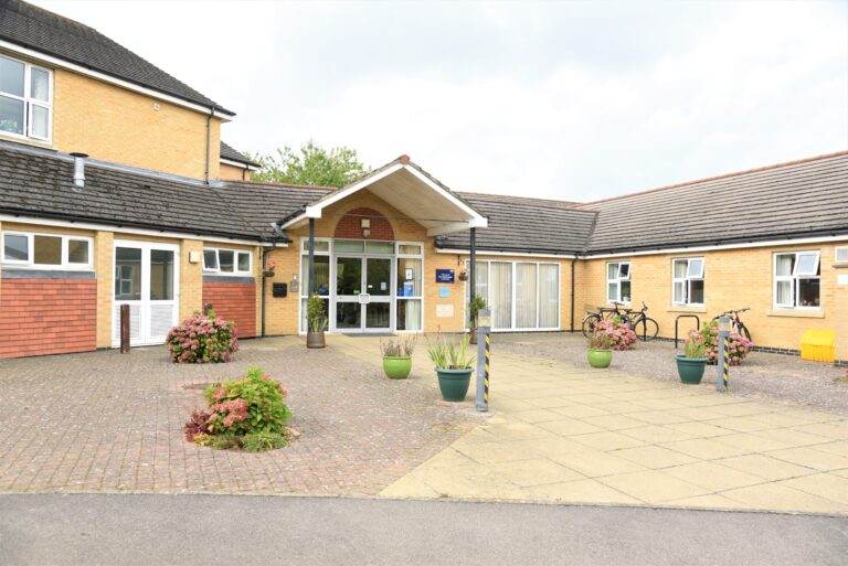 Entrance of the Headington Care Home featuring a welcoming façade, flowerpots, and a pathway leading to the main entrance.