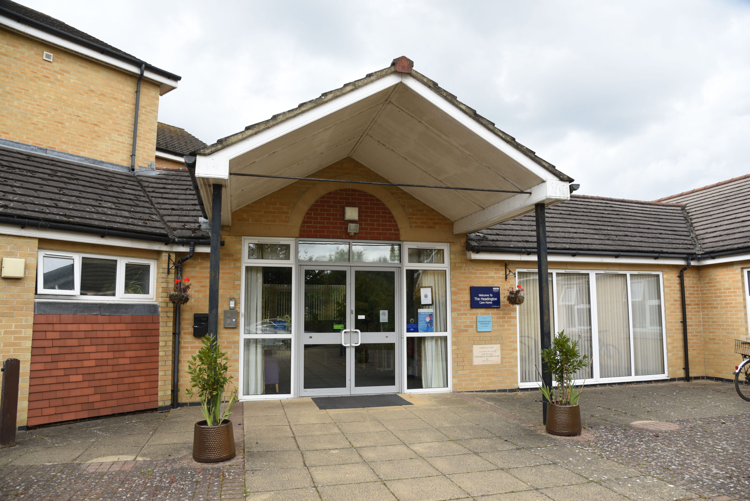 Entrance to the Headington Care Home features a welcoming porch, large glass doors, and potted plants on either side of the pathway.