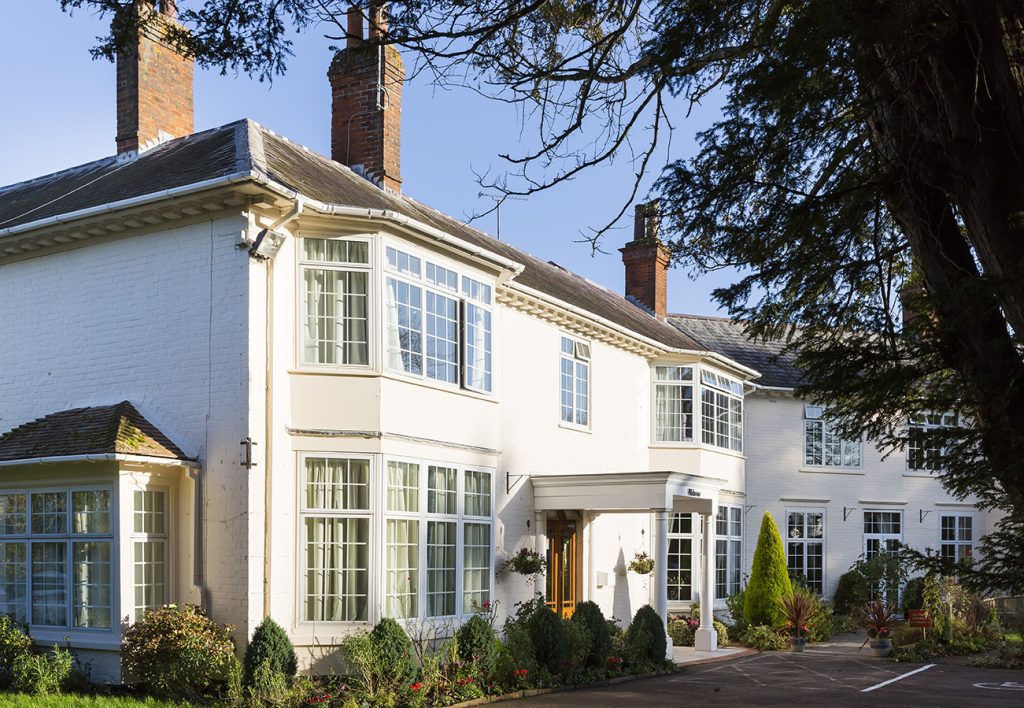 Bright, spacious care home with large windows, elegant architecture, and landscaped greenery in front, under a clear blue sky, Hungerford Care Home, a care home in Hungerford.