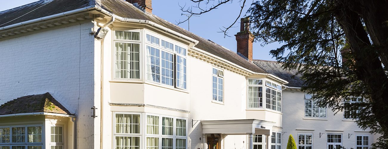 Bright, spacious care home with large windows, elegant architecture, and landscaped greenery in front, under a clear blue sky, Hungerford Care Home, a care home in Hungerford.