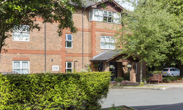 Brick building of Kingston Care Home with green foliage in front, a sign for private parking, and a well-kept outdoor space.