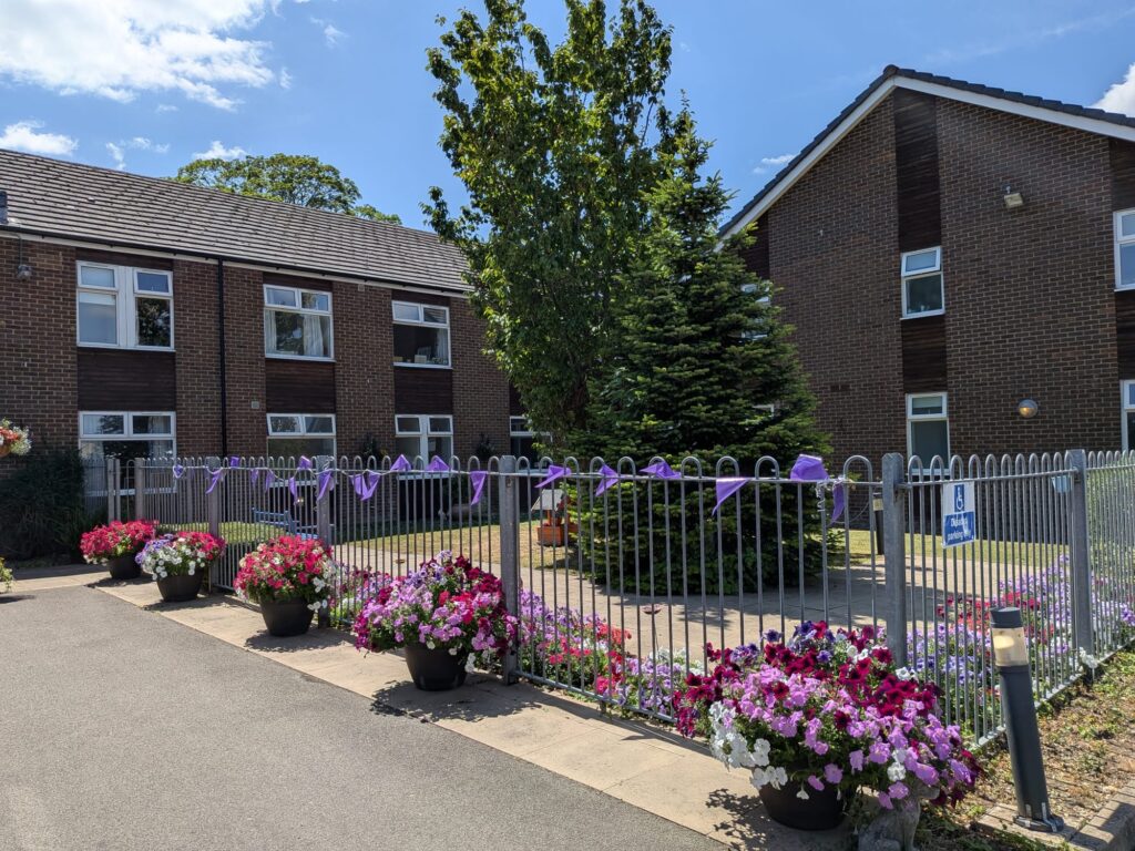 The brick exterior of Queensway House is lined with flower planters and purple ribbons, a care home in Hemel Hempstead.