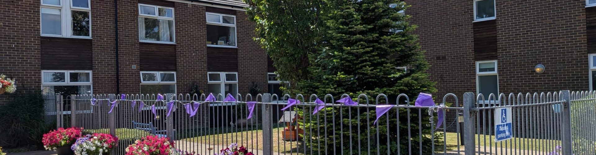 The brick exterior of Queensway House is lined with flower planters and purple ribbons, a care home in Hemel Hempstead.