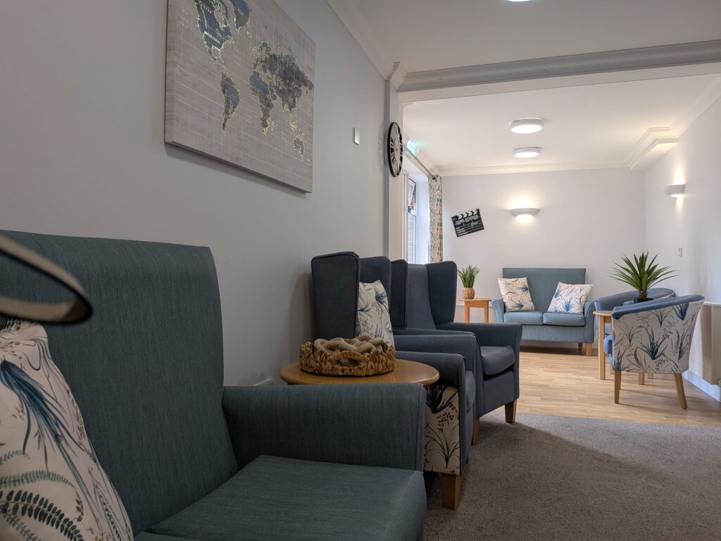 Queensway House sitting room with blue sofas, armchairs, potted plants and a world map.