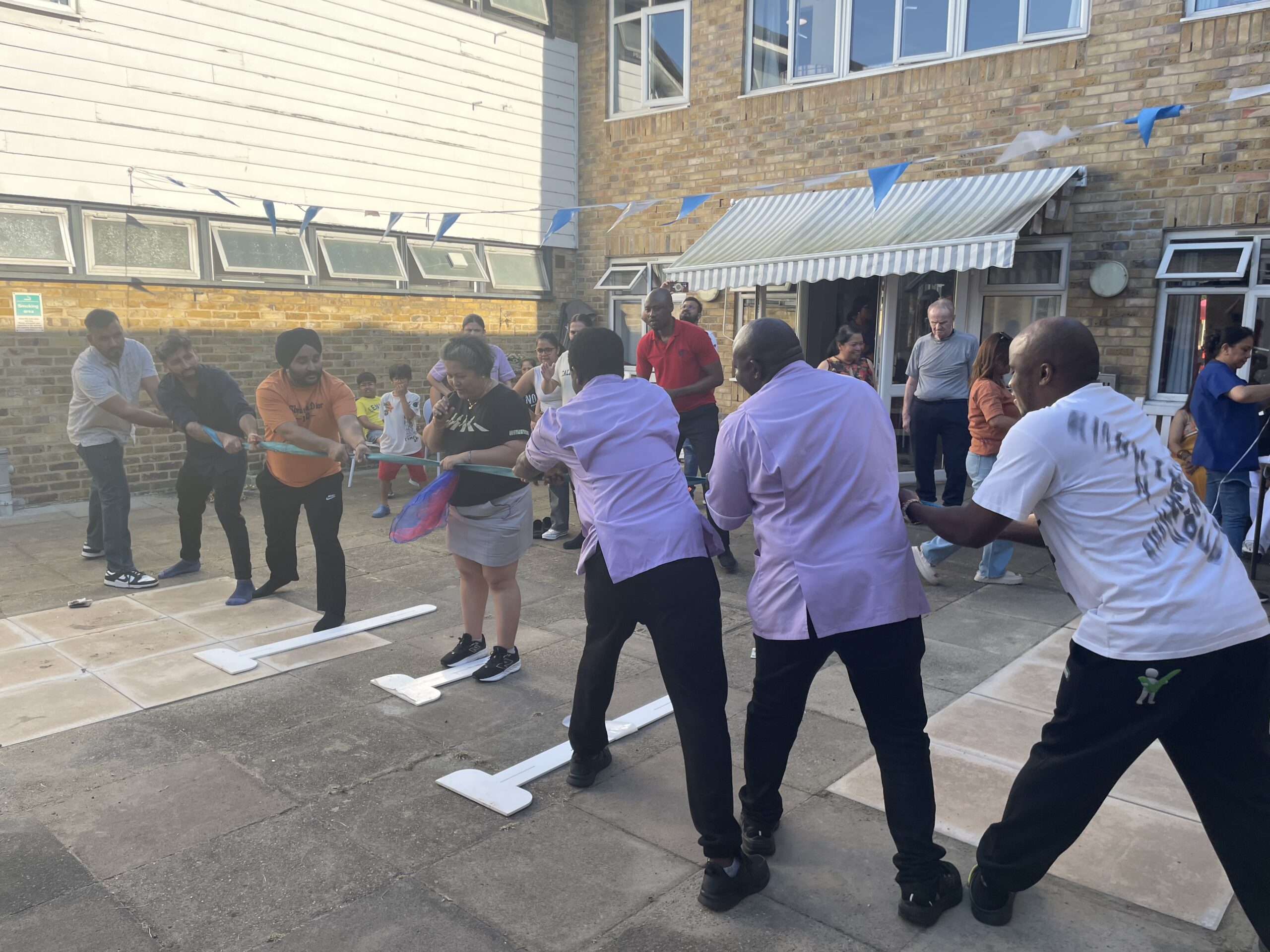 Residents and staff participate in a tug-of-war game outdoors, with colorful decorations and a lively atmosphere at Hillside Nursing Home.