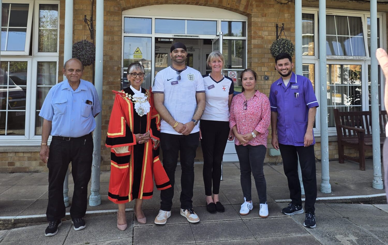 Care home staff posing outside brick building with residents