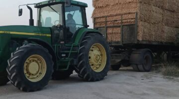 John Deere tractor hauling stacked hay bales on farm