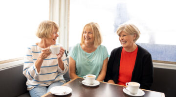 Three elderly friends enjoying tea together in a bright café